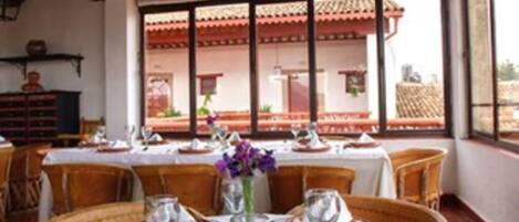 A dining area with round tables set for four, each with white tablecloths, brown plates, and silverware.