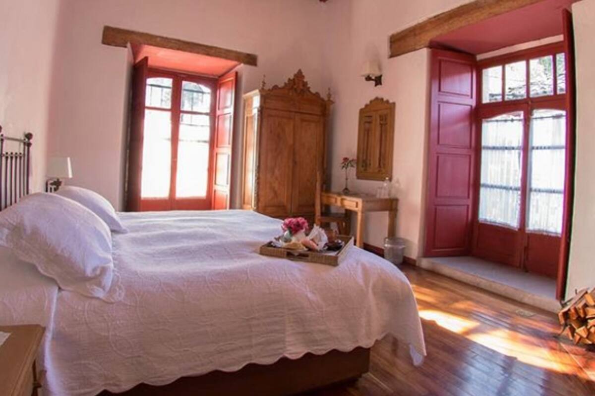 A bedroom with a wooden bed, a wooden wardrobe, and a window with red shutters.