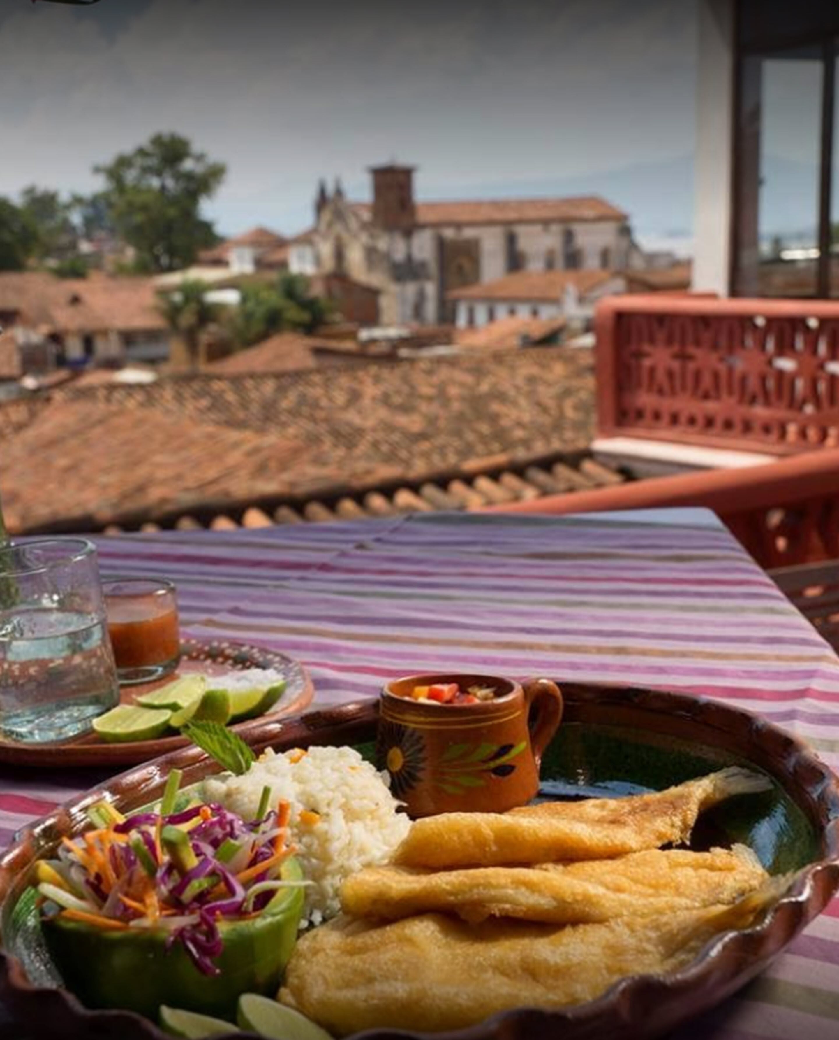 Una mesa con comida que incluye arroz, pescado frito y una ensalada, frente a un paisaje urbano.