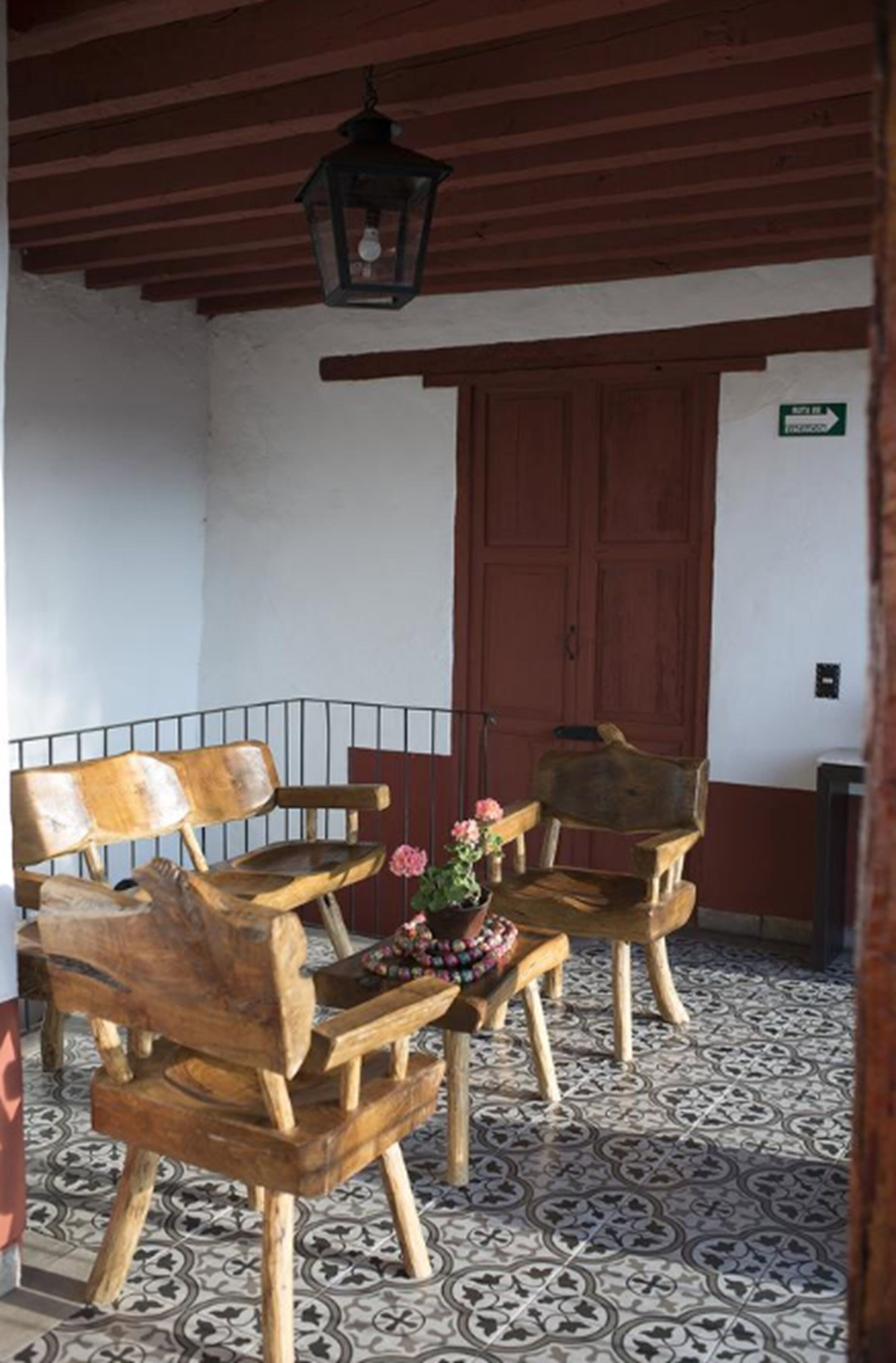 Un conjunto de banco y silla de madera sobre un suelo de baldosas, un farol colgante y una puerta con un letrero.