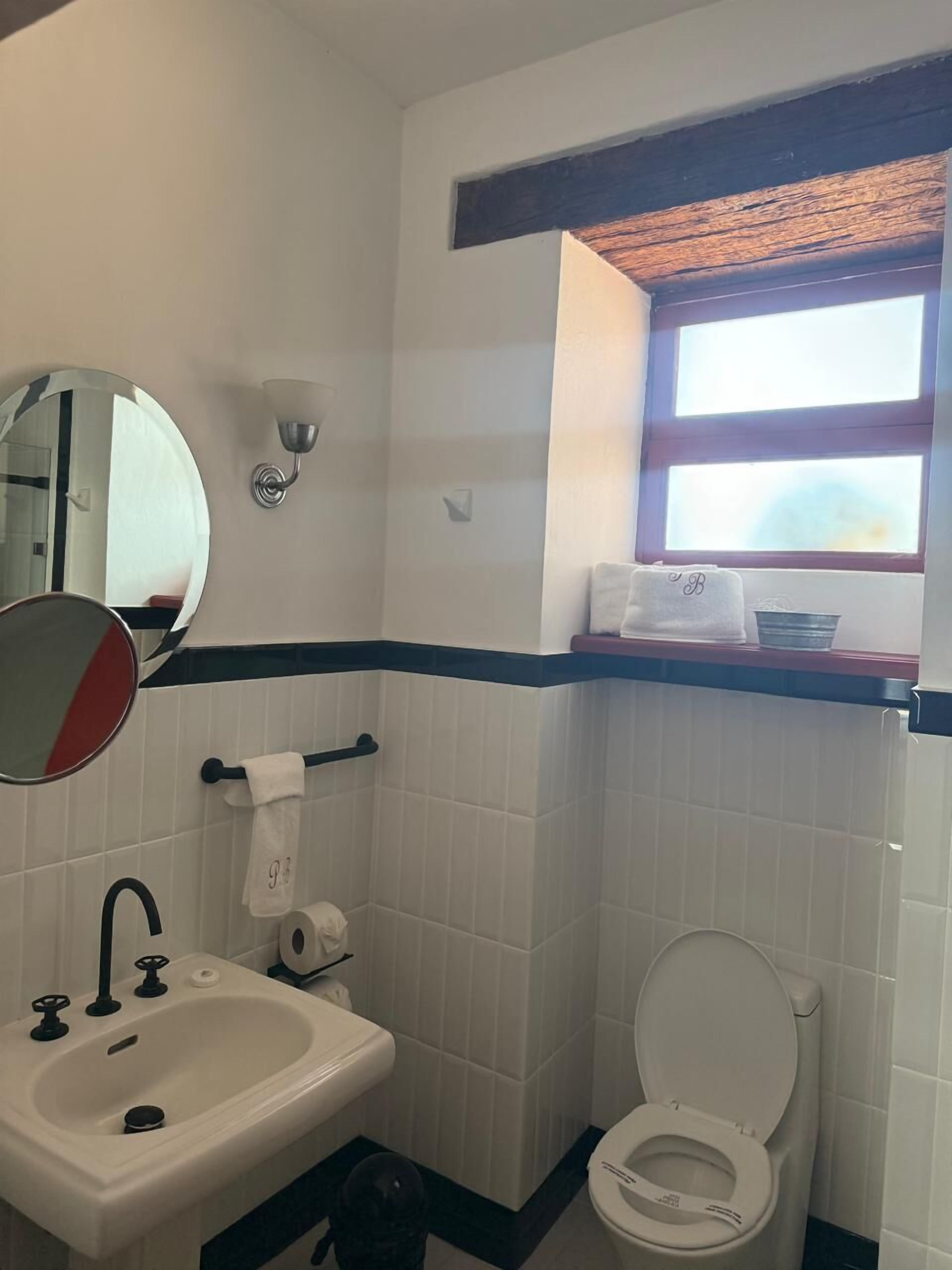 A bathroom with a sink, toilet, mirror, and a window above the toilet.