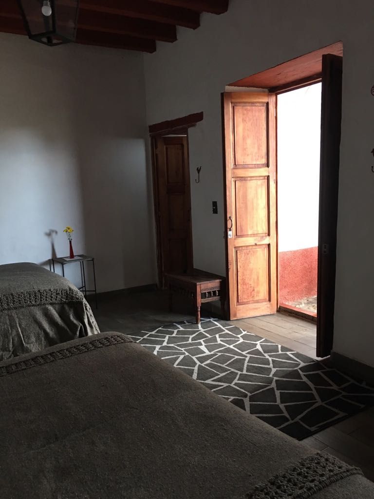 Un dormitorio con cama, un armario de madera, una mesita con un florero y una alfombra estampada.