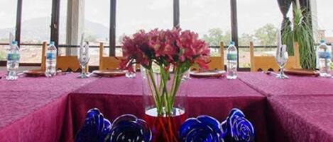 Comedor con mesas cubiertas de manteles rojos, un florero con flores y cristalería azul.