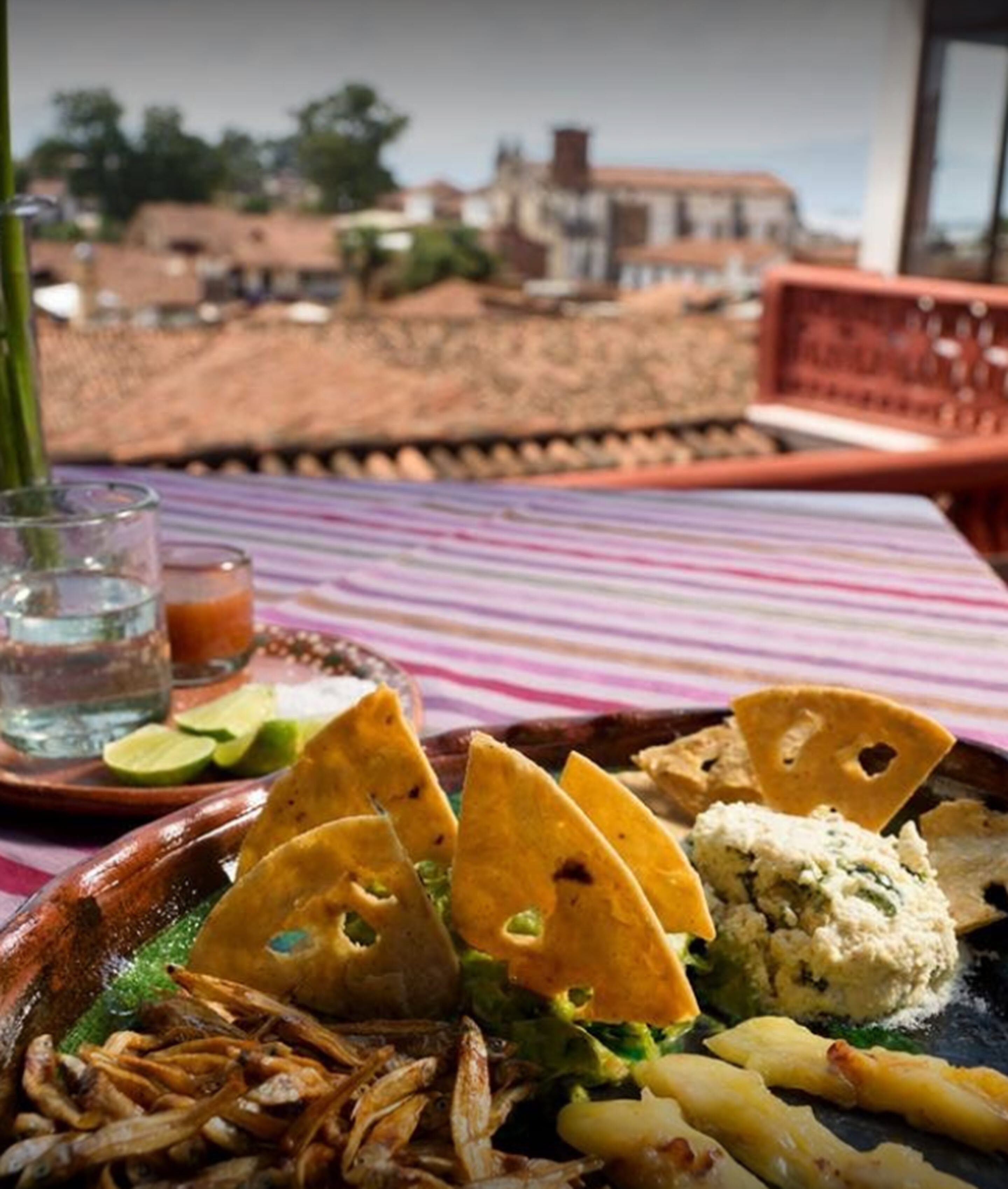 A table with a colorful striped tablecloth, a plate of food including tortilla chips, guacamole, and a green dip, and a glass of water.