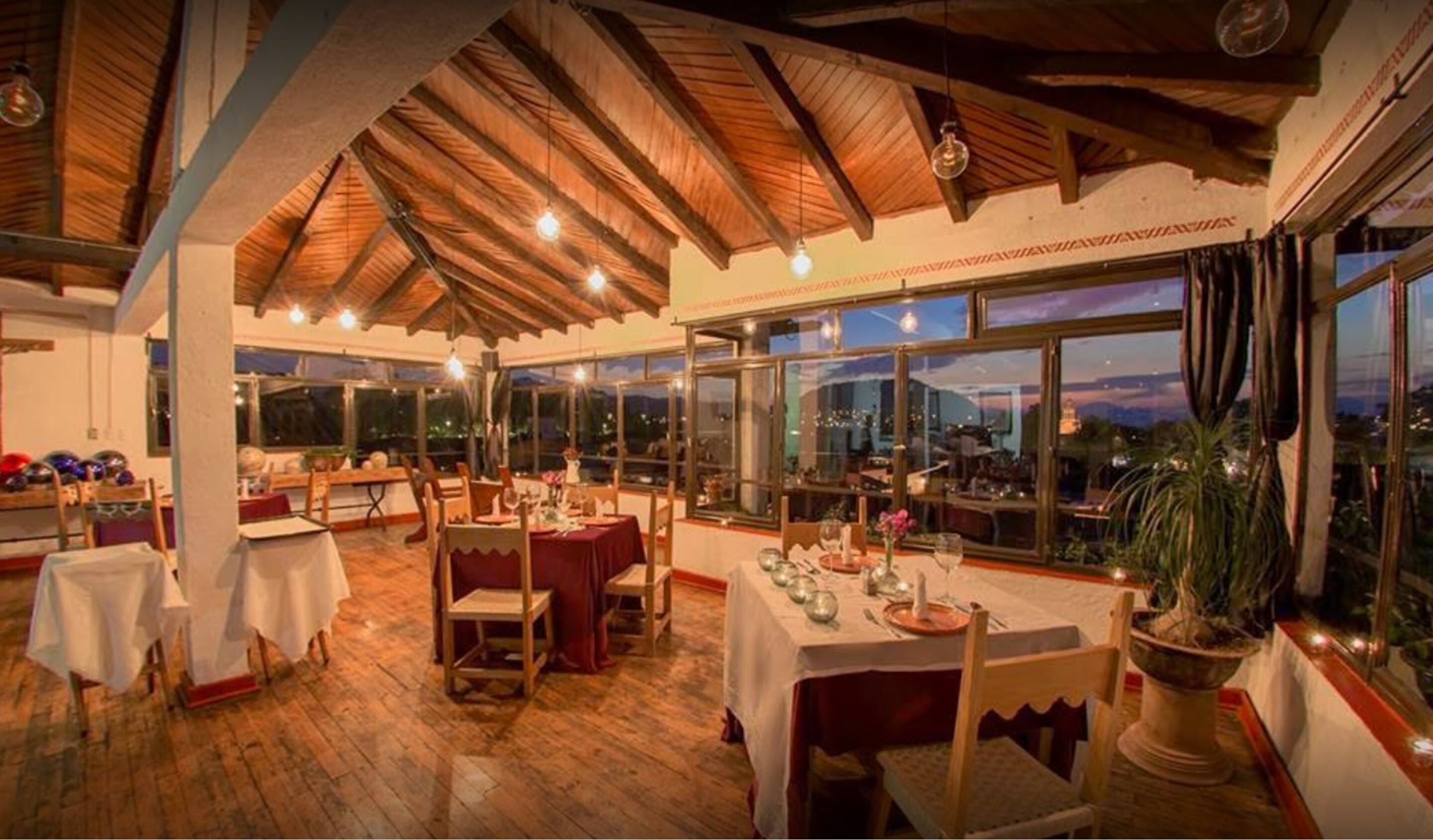 Un restaurante con vigas de madera, ventanas amplias y mesas dispuestas para comer.