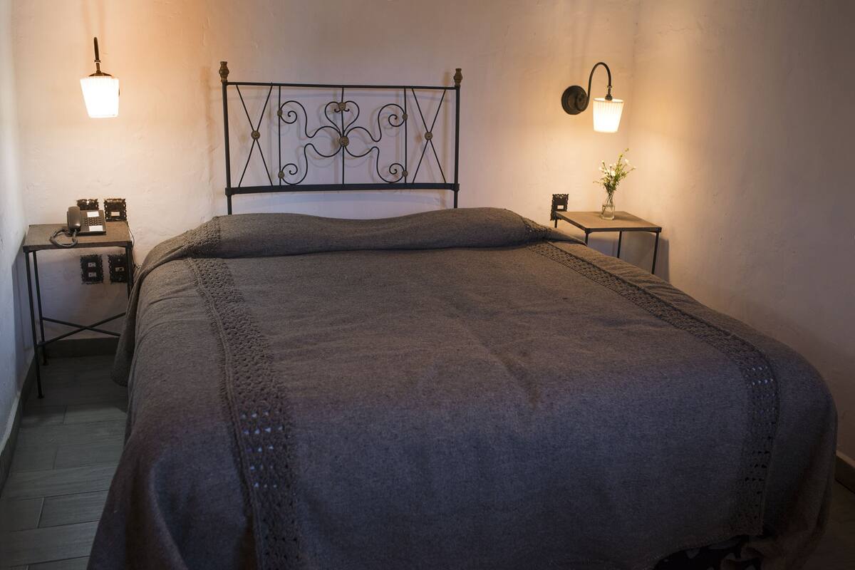 A neatly made bed with a metal headboard, two bedside tables with lamps, and a small vase with flowers on one table.