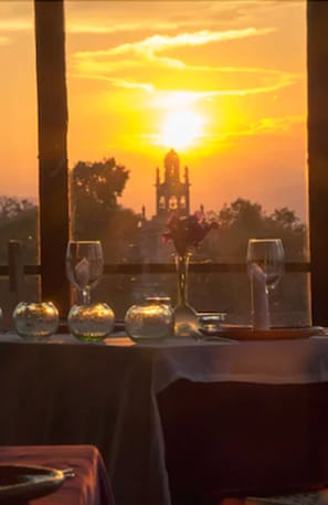 Une table dressée pour un repas, avec en toile de fond un coucher de soleil et un clocher.