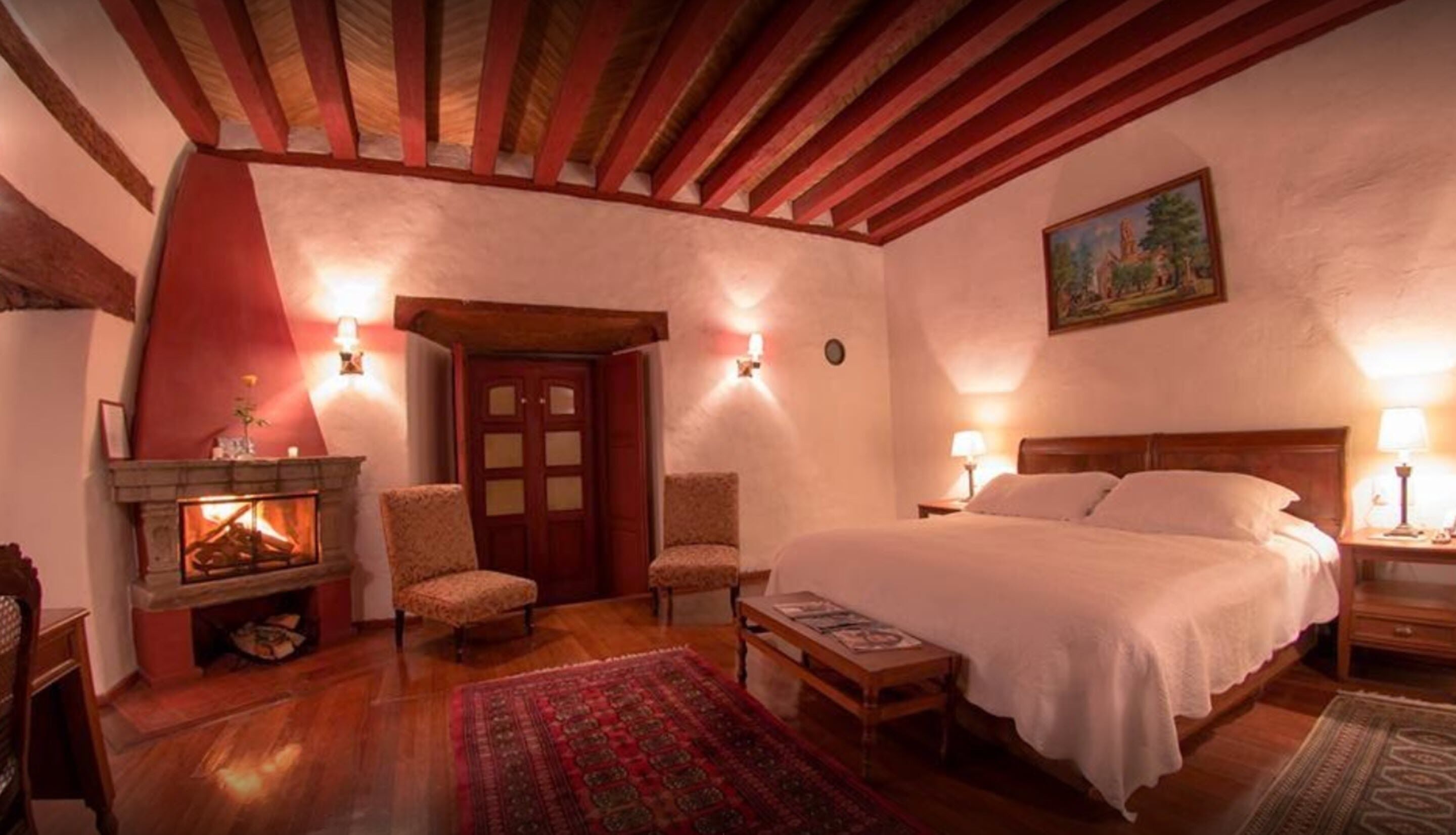 A cozy bedroom with a fireplace, a large bed, and a wooden ceiling.