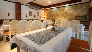 A dining area with white tables and chairs, a patterned table runner, and a stone wall in the background. - Vansana Vientiane - Ban Phonthan (Vientiane)