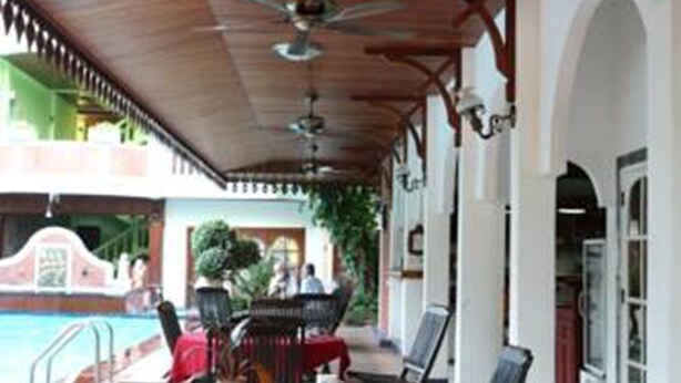 A covered outdoor dining area with tables and chairs, a pool in the background, and a ceiling fan. - Vansana Vientiane - Ban Phonthan (Vientiane)