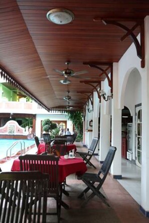 A covered outdoor dining area with tables and chairs, a pool in the background, and a ceiling fan. - Vansana Vientiane - Ban Phonthan (Vientiane)