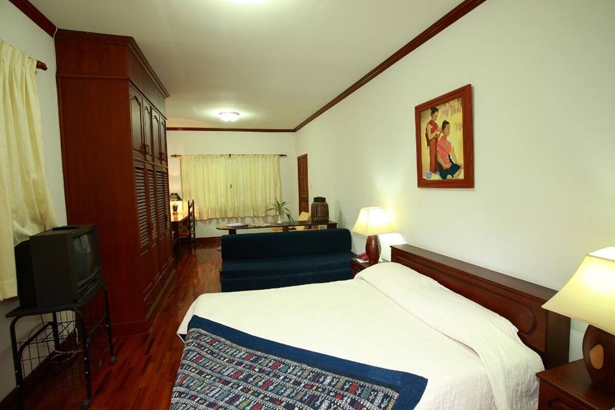 A hotel room with a bed, a desk with a television, a chair, a lamp, and a painting on the wall.