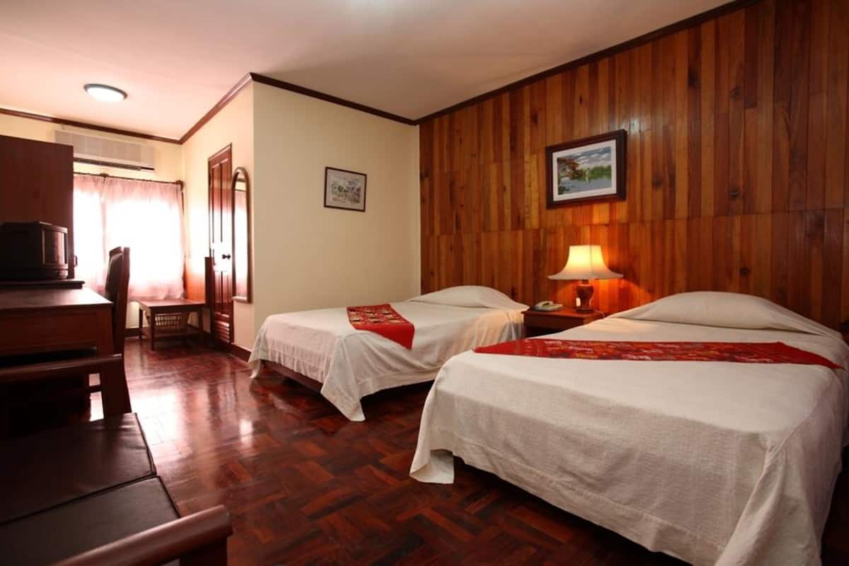 A hotel room with two single beds, a desk with a chair, a lamp, and a wooden wall.