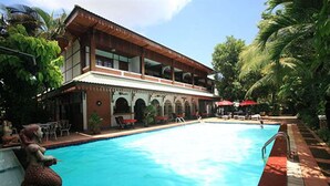 A swimming pool with a two-story building in the background, surrounded by palm trees and outdoor seating. - Vansana Vientiane - Ban Phonthan (Vientiane)