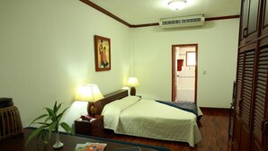A hotel room with a bed, bedside lamps, a small table with a plant and a magazine, a door, and a wall-mounted air conditioner. - Vansana Vientiane - Ban Phonthan (Vientiane)