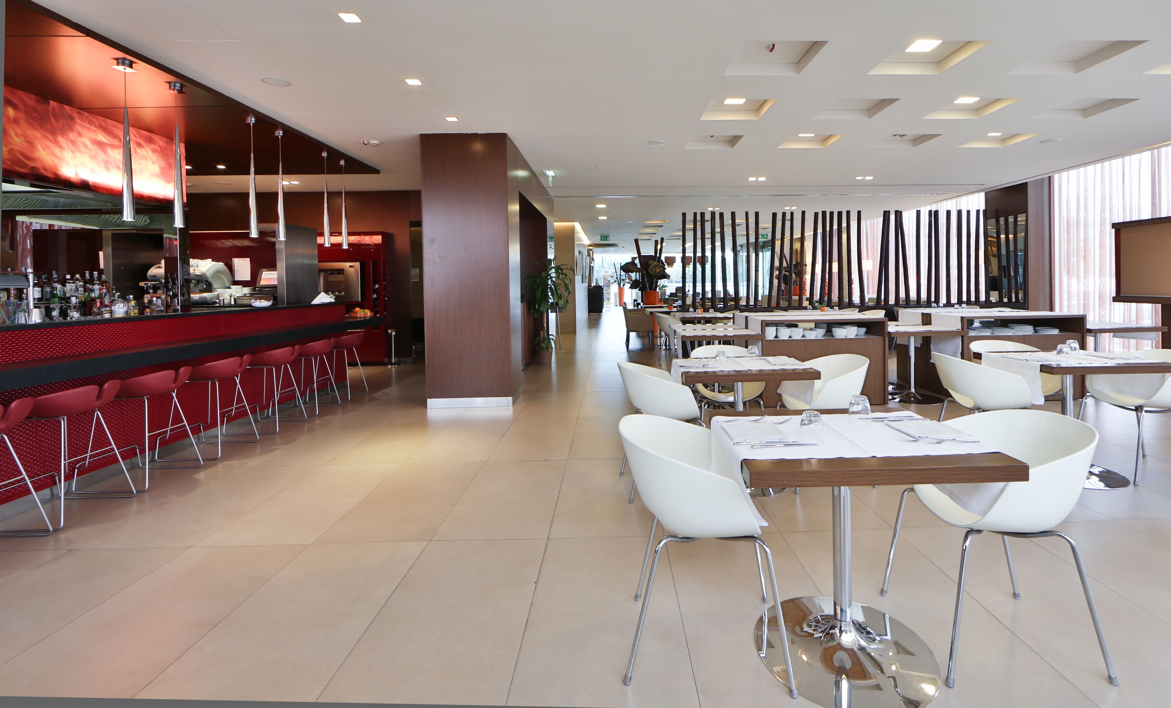 Un restaurante moderno con taburetes rojos, mesas blancas y una variedad de disposiciones de asientos.