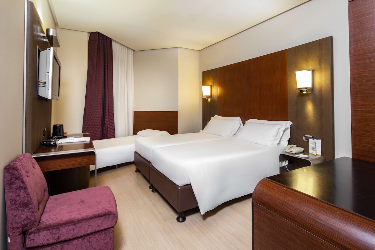 Une chambre d’hôtel avec un lit double, un bureau avec une chaise, une télévision et une table de chevet avec une lampe.