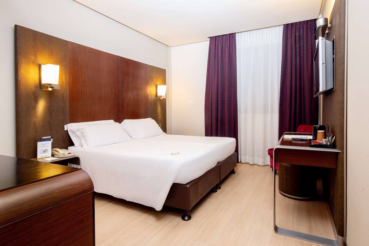 Une chambre d’hôtel comprenant un lit, une table de chevet, une lampe et un bureau avec une chaise.