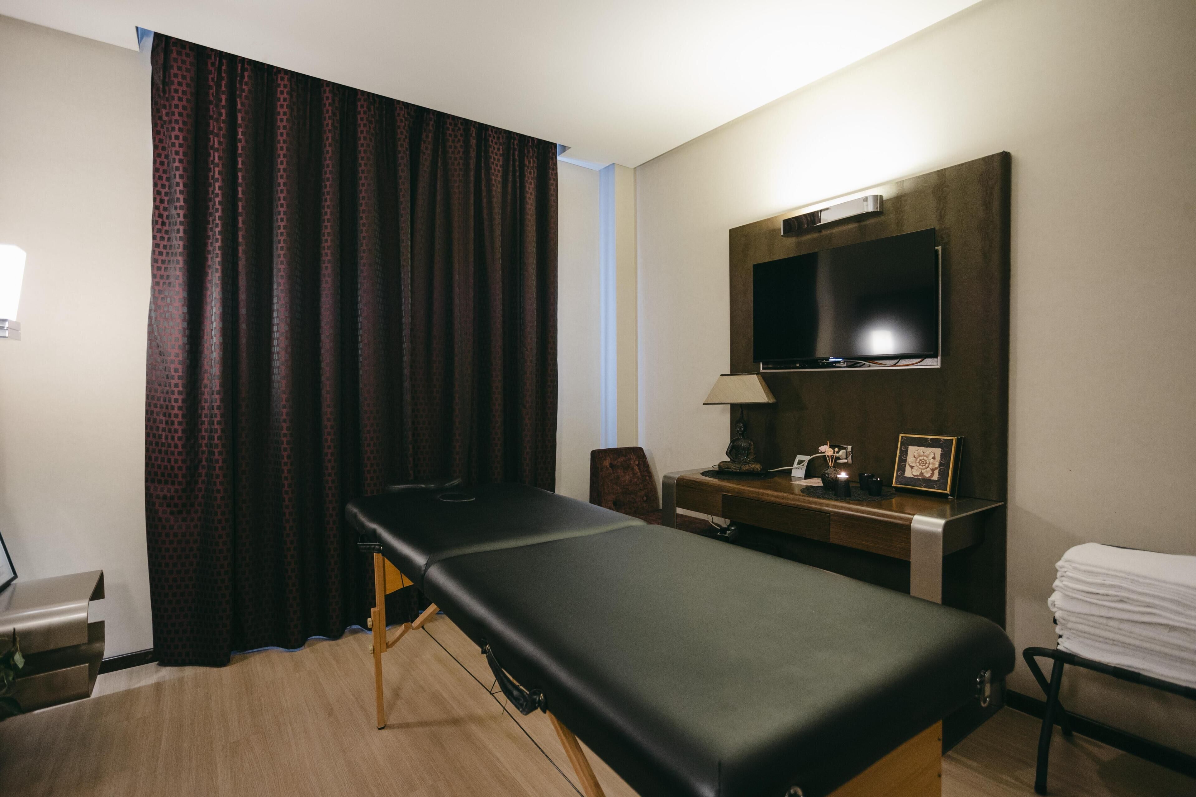 Une pièce comprenant une table de massage, un téléviseur fixé au mur, un bureau avec une lampe et une chaise.