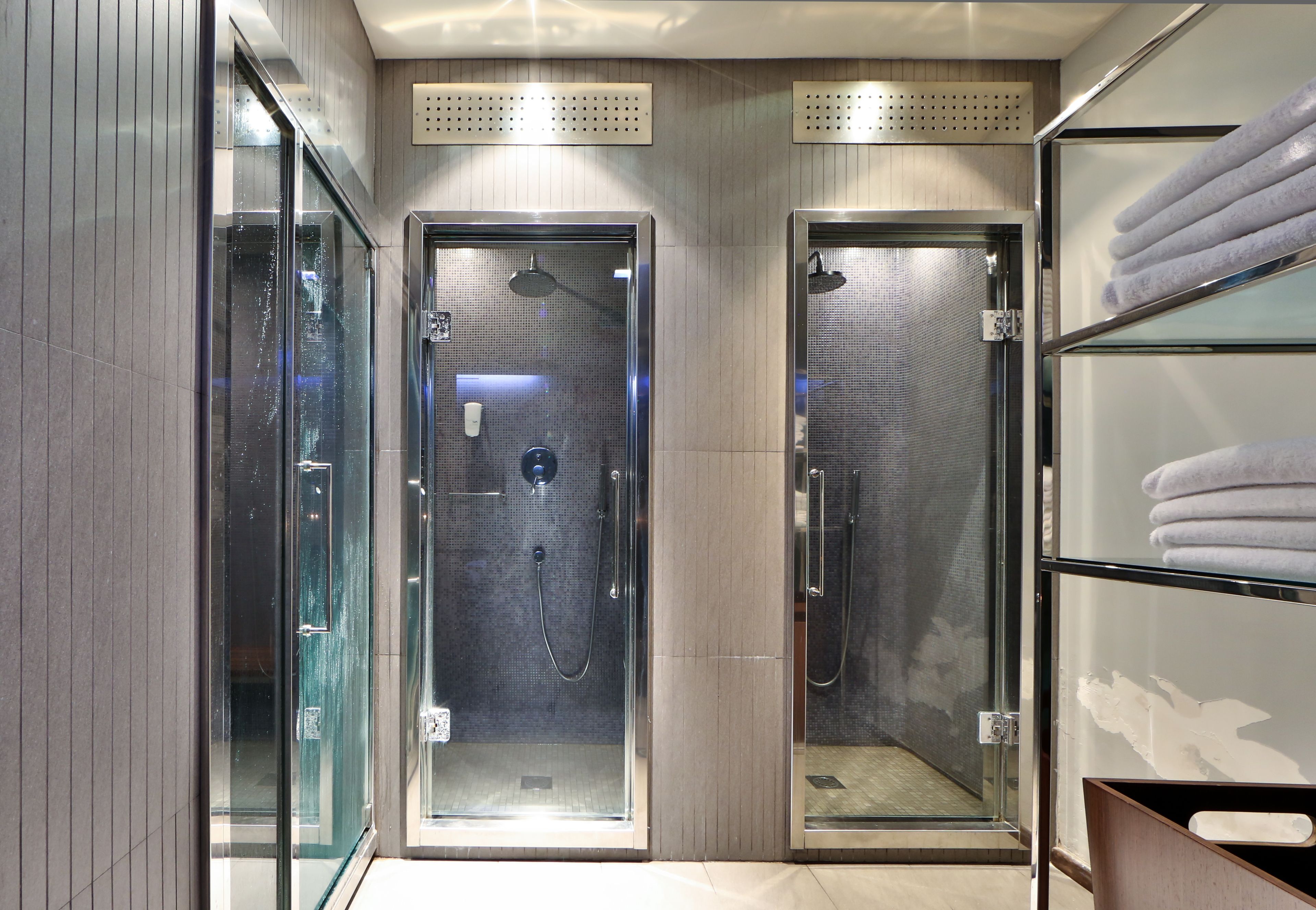 A modern bathroom with two glass-enclosed shower stalls, a towel rack, and a wooden panel wall.