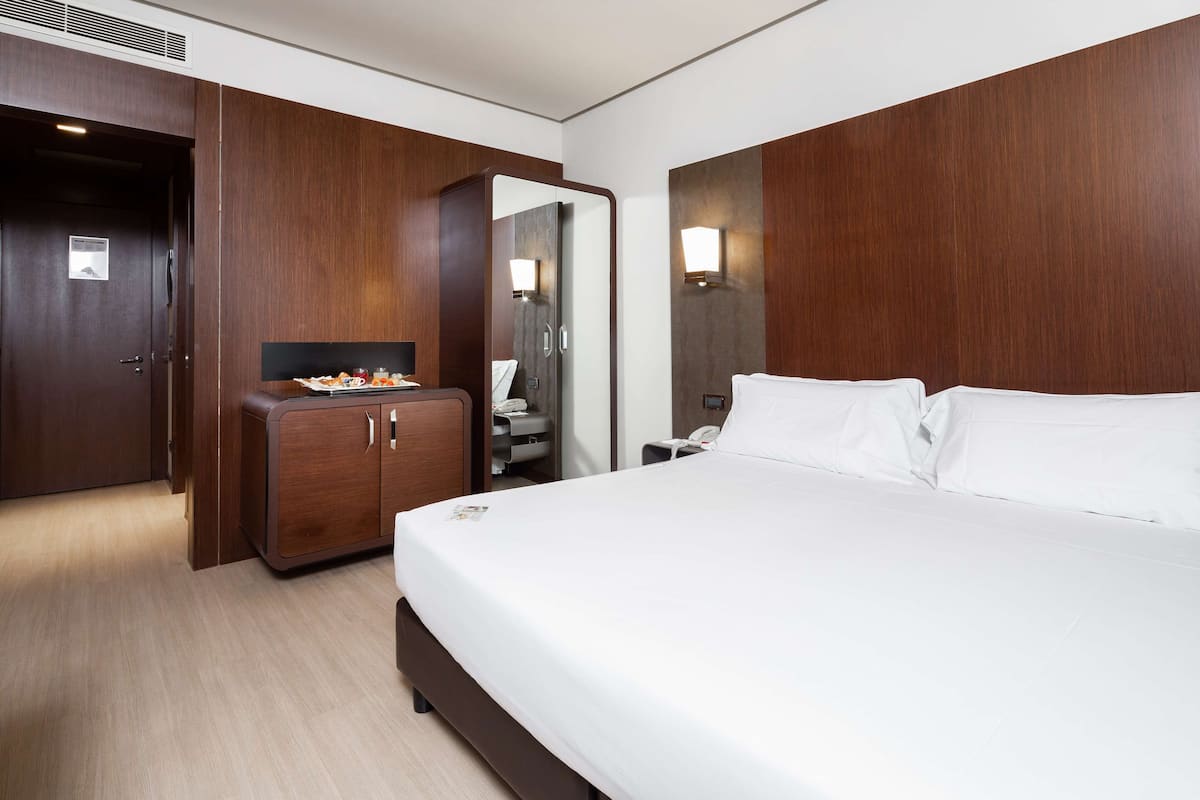 Une chambre d’hôtel avec un grand lit, une armoire en bois, un miroir et une petite table avec des en-cas.