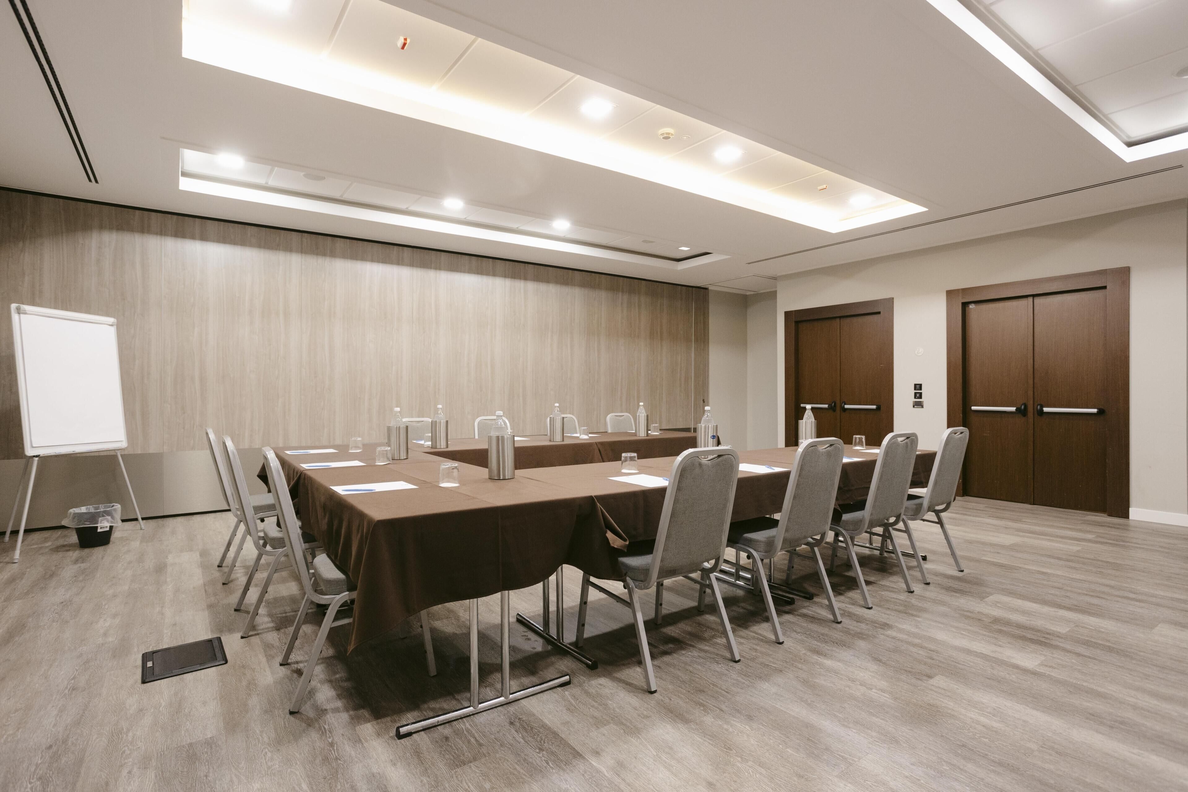 Une salle de conférence avec une longue table, des chaises, un tableau blanc et une porte.