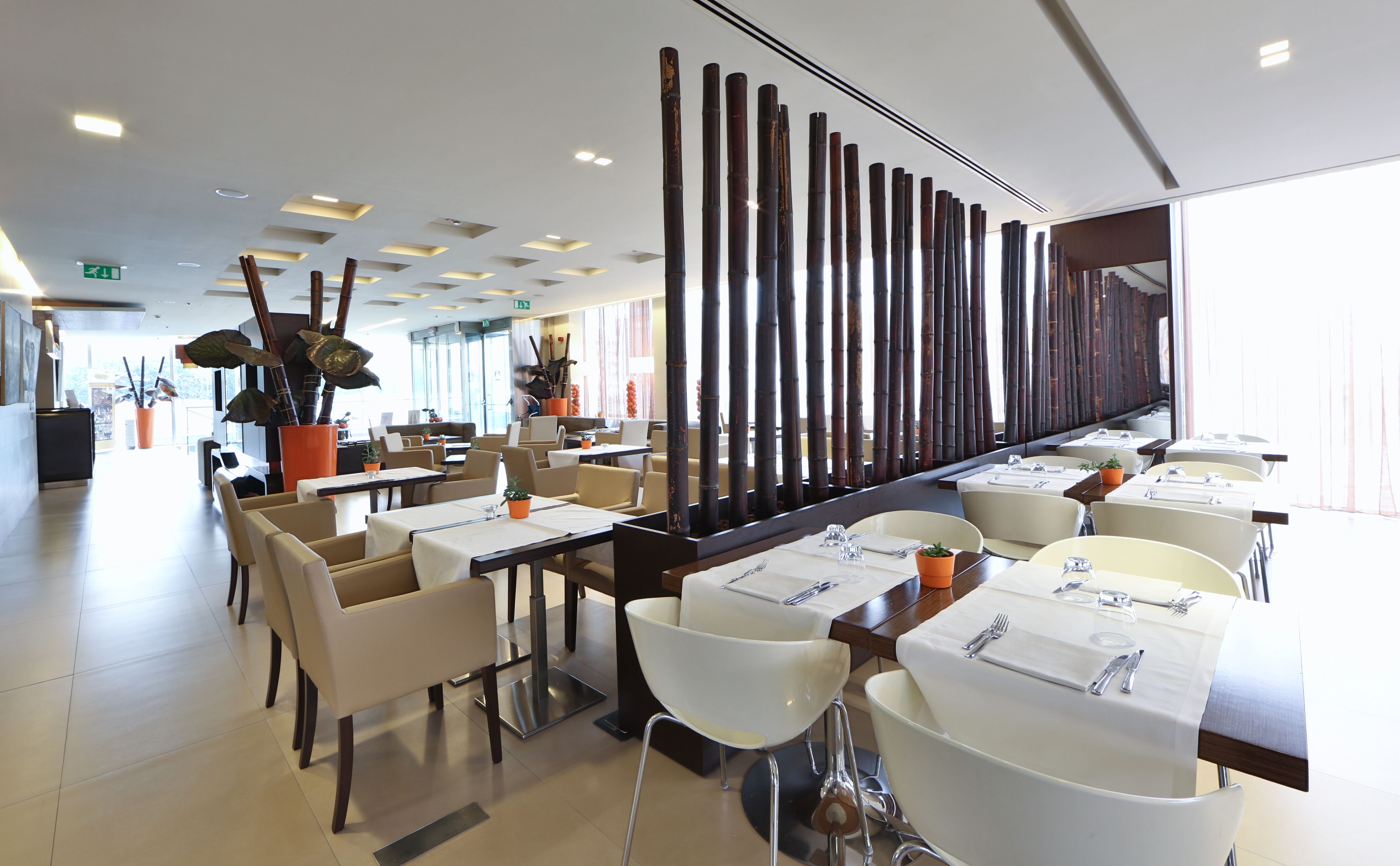 Interior moderno de restaurante con mesas altas, asientos cómodos y una pared decorativa de bambú.