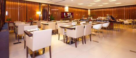 A spacious hotel dining area with multiple tables and chairs, a buffet station, and a reception desk.