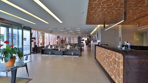 Een moderne hotellobby met een receptiebalie, een zithoek en grote ramen.