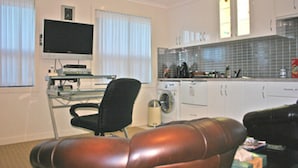 Een moderne keuken met een wasmachine, een zithoek met een leren bank en een flatscreen televisie op een standaard.