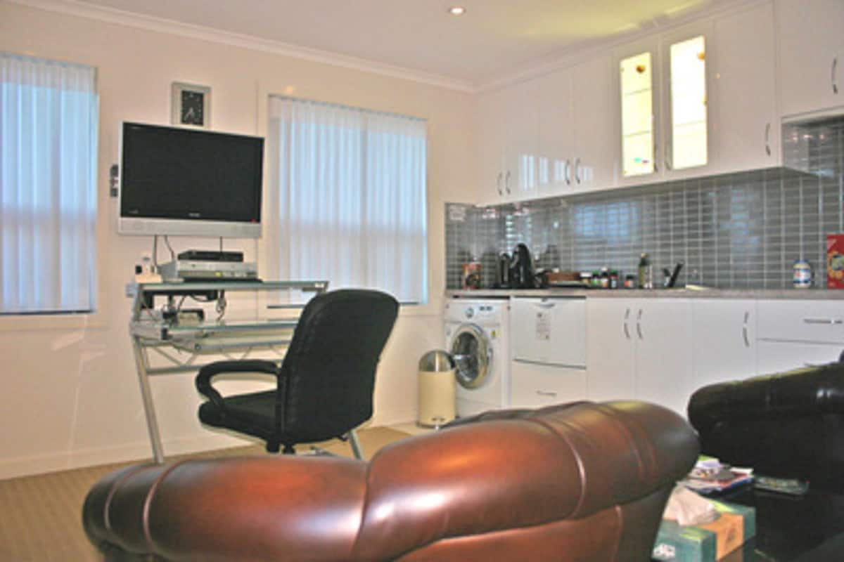 A modern kitchen with a washing machine, a dining area with a leather couch, and a flat-screen TV on a stand.