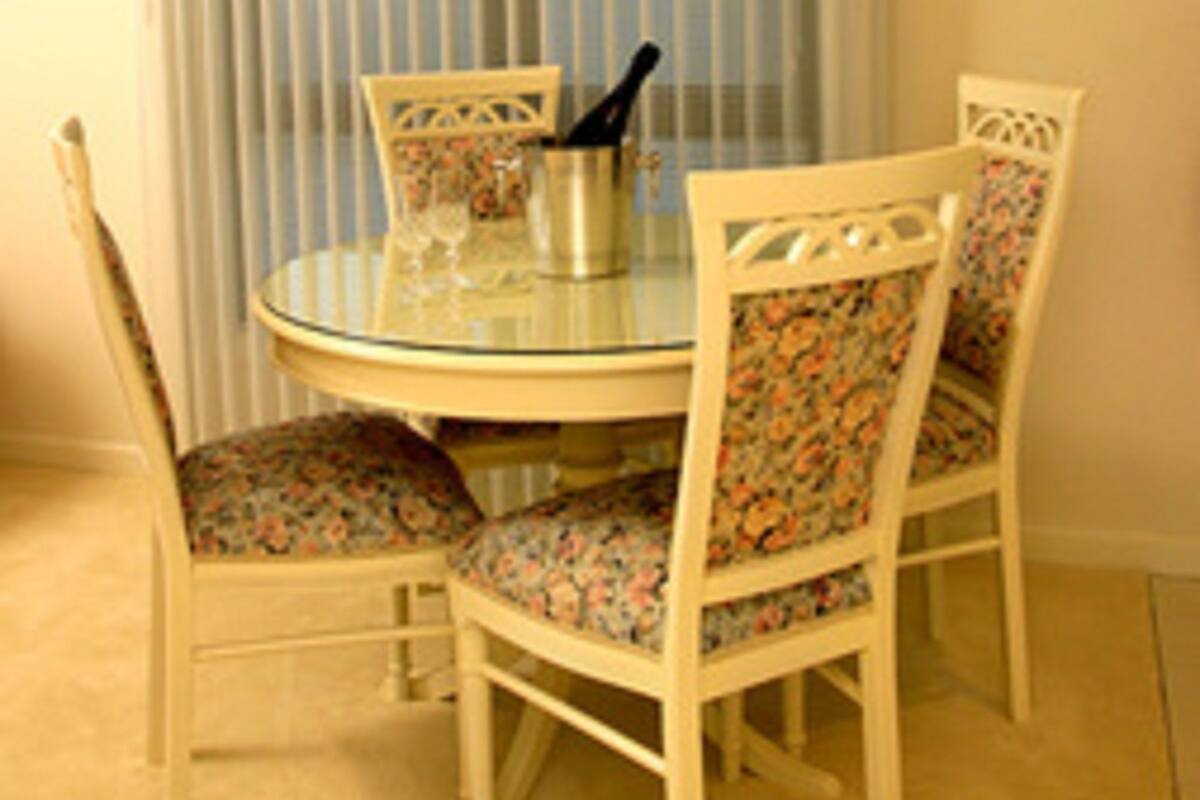 A dining area with a round glass table, floral upholstered chairs, and a bottle of champagne.