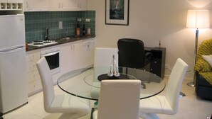 Een moderne keuken met witte kasten, een glazen eettafel en een zwarte bureaustoel.