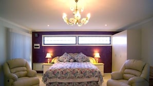 Een slaapkamer met een bed, twee stoelen, een kroonluchter en een raam met jaloezieën.
