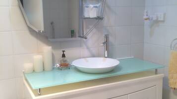 Un baño con un lavabo blanco, un estante de vidrio arriba y un espejo.