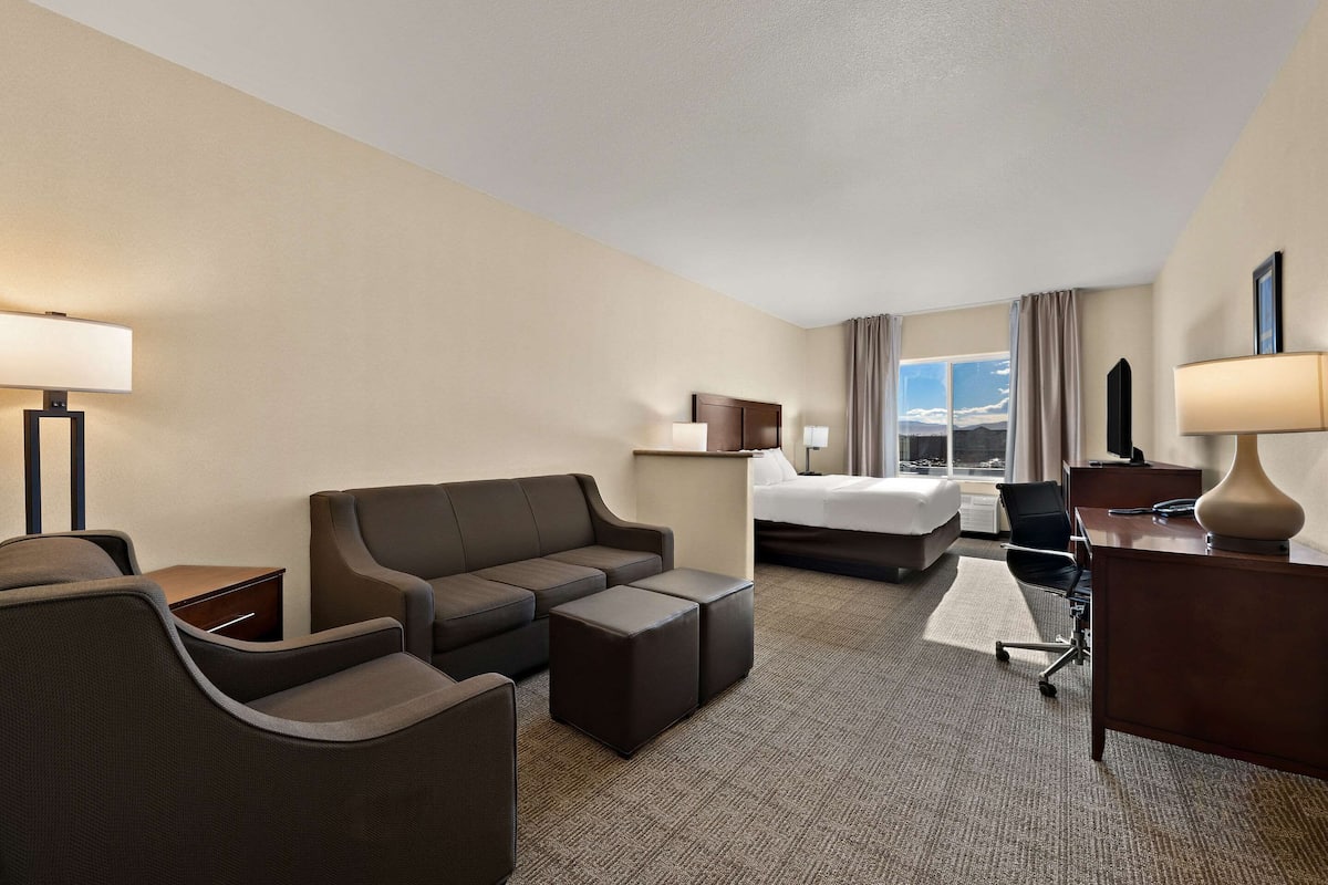 A hotel room with a sofa, ottoman, desk, and a bed.