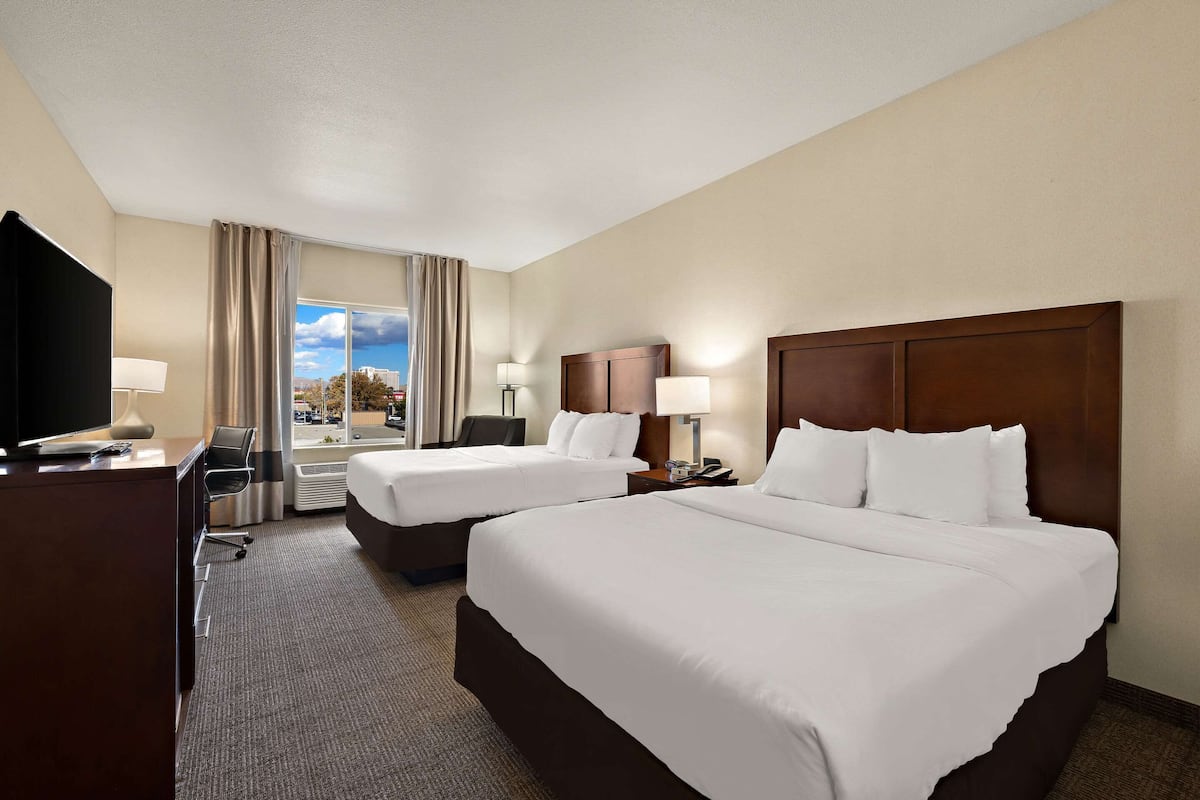A hotel room with two beds, a desk with a TV, a chair, and a window with curtains.