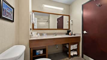 A hotel bathroom with a wooden vanity, a large mirror, a toilet, and a shower area.