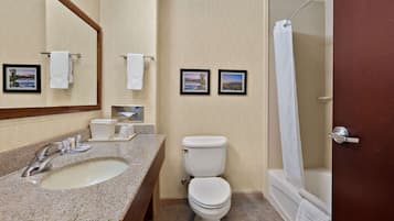 Un baño con lavamanos, inodoro y ducha. Hay toallas colgadas en la pared y un marco de fotos.