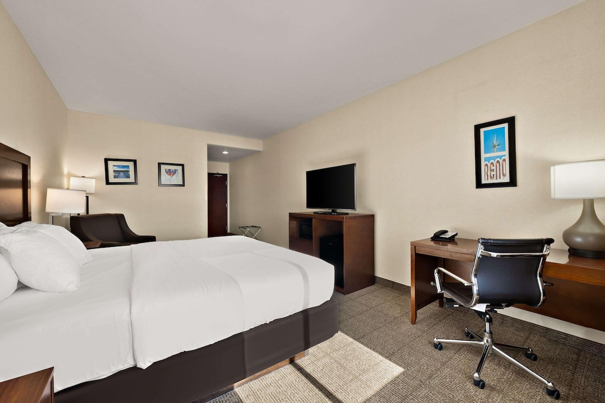 A hotel room with a bed, desk, chair, TV, and framed pictures on the wall.
