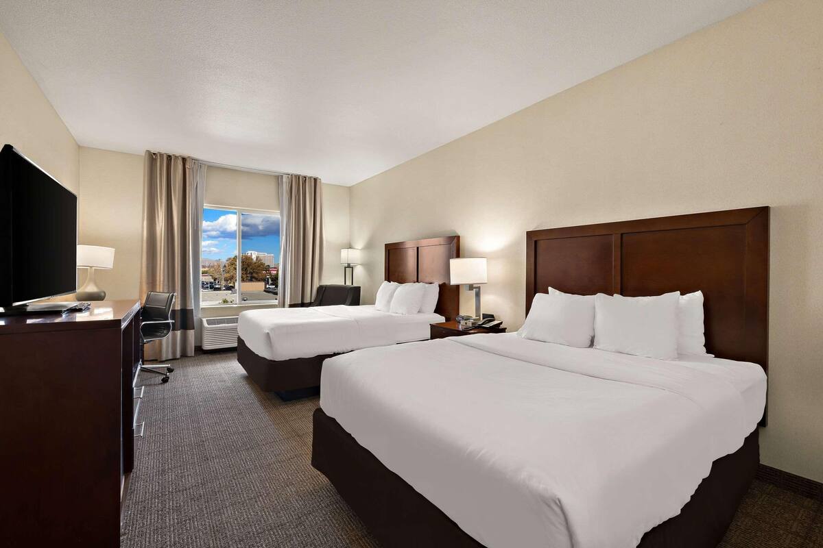 A hotel room with two beds, a desk, a TV, and a window with curtains.