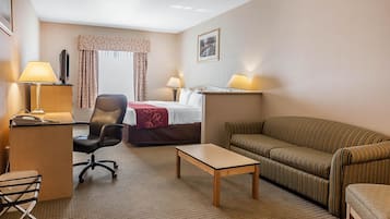 A hotel room with a bed, a sofa, a desk with a lamp, a chair, and a small table.