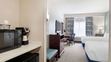 Una habitación de hotel con cama, escritorio, computadora, microondas y cafetera.