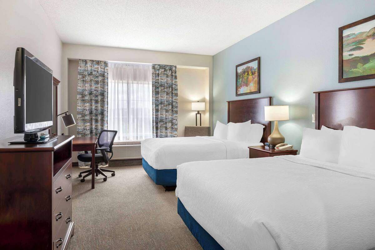 A hotel room with two beds, a desk with a computer, a TV, and a window with curtains.