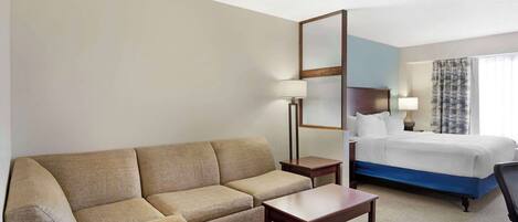 A hotel room with a sofa, a small table, a bed, and a nightstand.