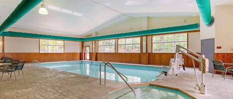 Una piscina interior con tabla de salto, silla de socorrista y zona de estar con mesas y sillas.