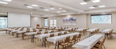 A conference room with multiple tables and chairs, a projector screen, and a large window.
