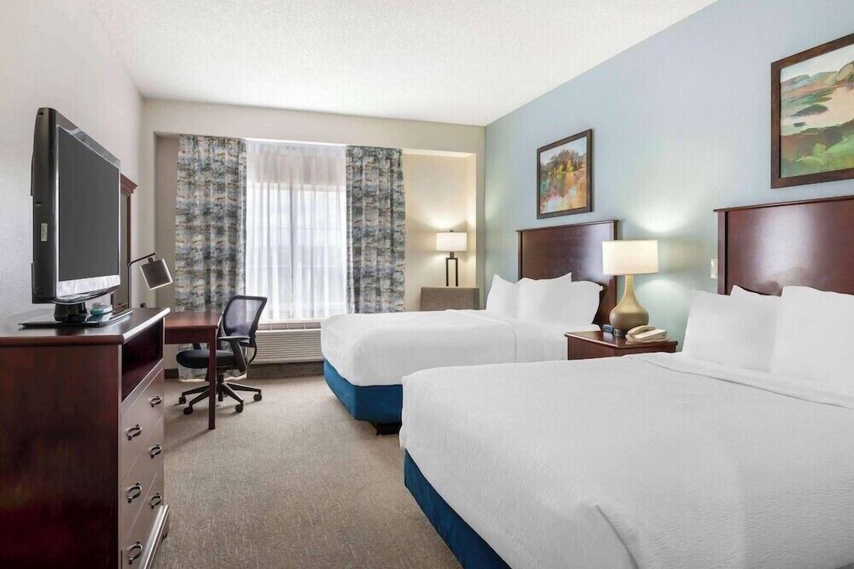 A hotel room with two beds, a desk with a computer, a TV, and a window with curtains.
