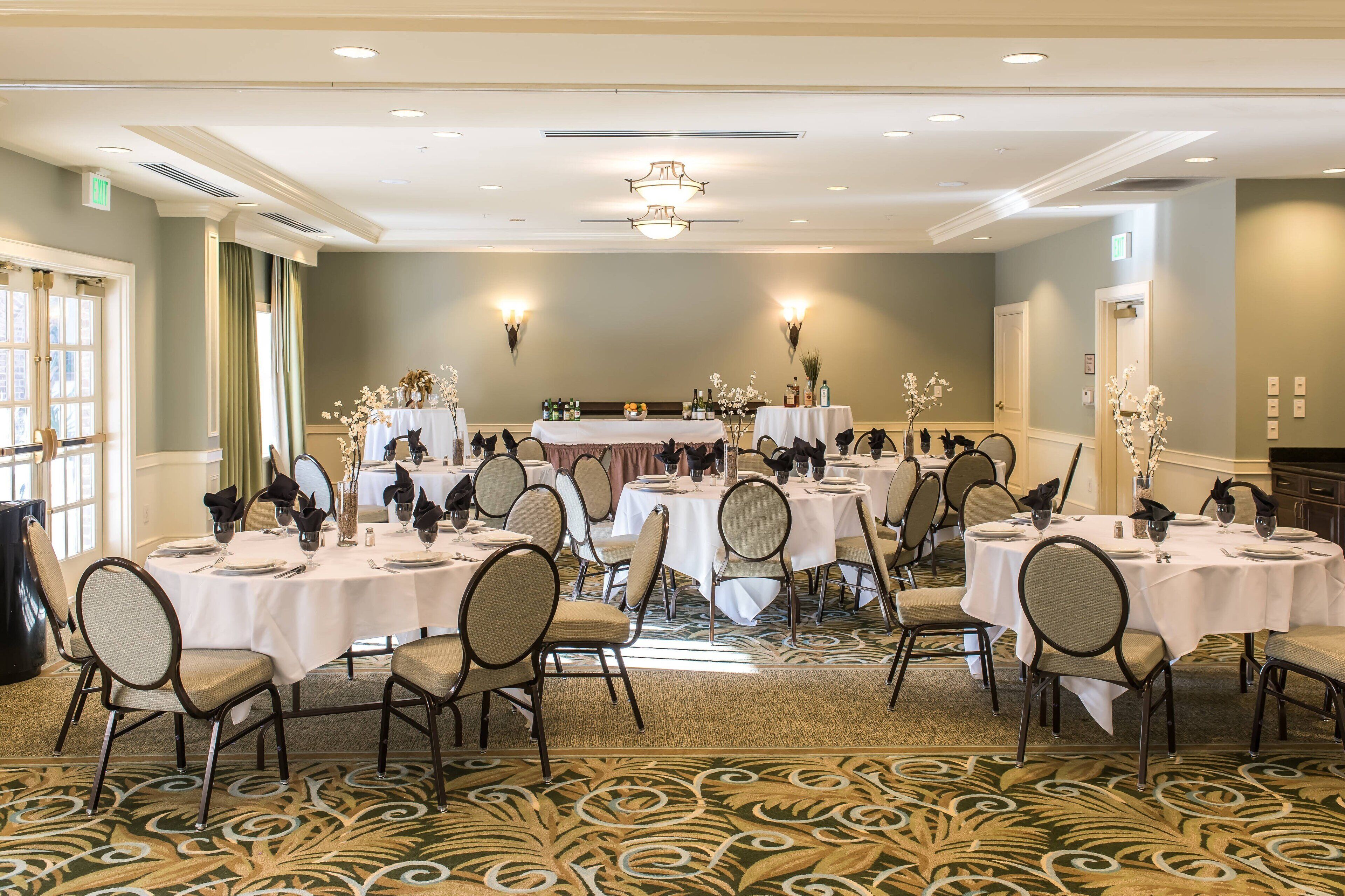 A banquet hall with round tables set for dining, chairs, and a stage with floral arrangements.