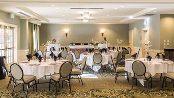 A banquet hall with round tables set for dining, chairs, and a stage with floral arrangements.